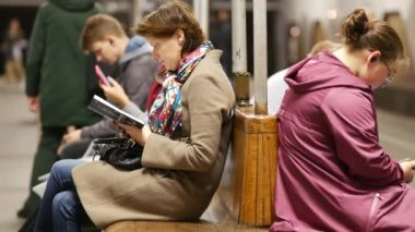 Metro istasyonundaki insanlar ahşap banklarda oturmuş treni bekliyorlar.