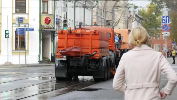 Oranje besproeiingsmachine rijdt langs de straat. De waterstralen zijn onderweg. Voertuig — Stockvideo