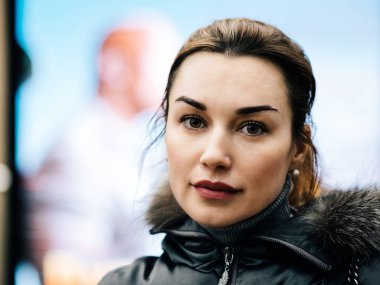 Genç bir kadın kameraya bakıyor. Saçlarını toplamış güzel bir kız