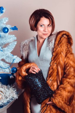 Tilki kürkü ve el çantası giymiş zarif bir bayan yılbaşı ağacının yanında duruyor.. 