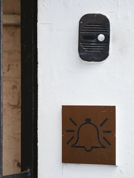 Die Gegensprechanlage an der weißen Wand des Hauses und das Emblem mit einem Glockensymbol. Gegensprechanlage mit einer Ruftaste und einem Schild mit einem Klingelbild. Anrufkommunikationsgerät soll in Mehrfamilienhaus eindringen. — Stockfoto