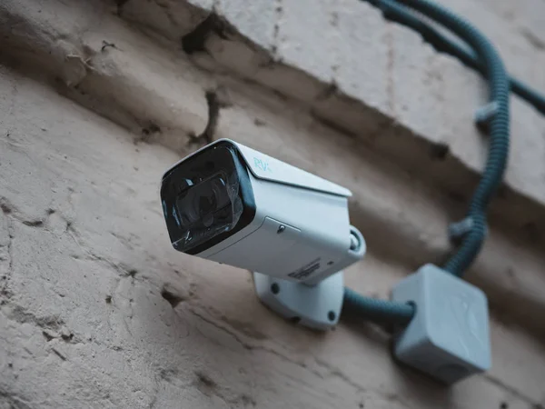 Telecamera a circuito chiuso esterna montata sulla parete di una vecchia casa di mattoni. Nuova fotocamera con pellicole protettive sull'obiettivo. Videosorveglianza in una strada cittadina . — Foto Stock