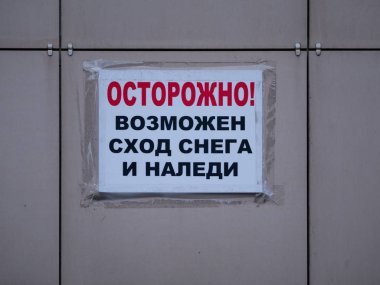 Duvara yapıştırılmış kağıttan bir mesaj yapıştırılmış ve üzerinde Rusça uyarı yazılı bir bant var. Dikkat, kar ve buz dışarı çıkabilir. Moskova, Rusya