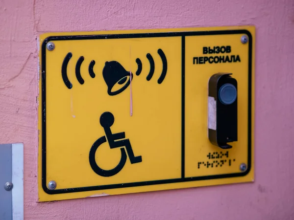 建物のピンクの壁には 車椅子のロゴとスタッフのためのコールボタンが付いています 鐘とインターホン付きの黄色の長方形のプレート — ストック写真