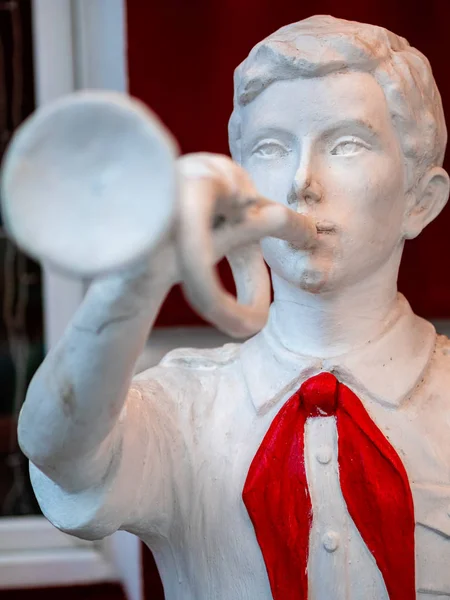 The figure of a pioneer with clarion in his hand near building. White sculpture of a boy with a red tie from the time of the Soviet Union era. Vintage silhouette of white plaster in Moscow, Russia