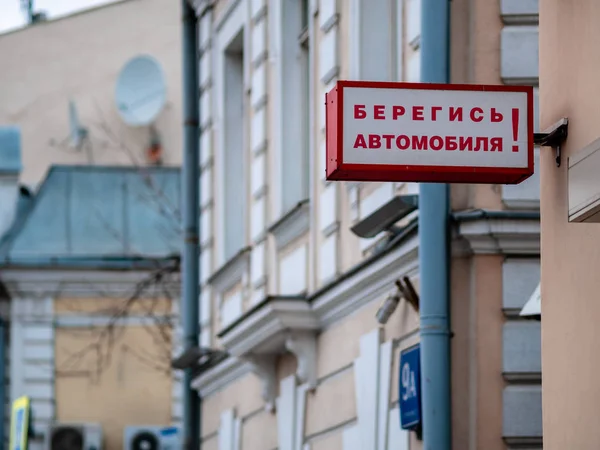 Street signboard plate with the inscription Beware of the car in Russian on an old building in the city center. White sign in a rectangular red case with backlight. Moscow, Russia