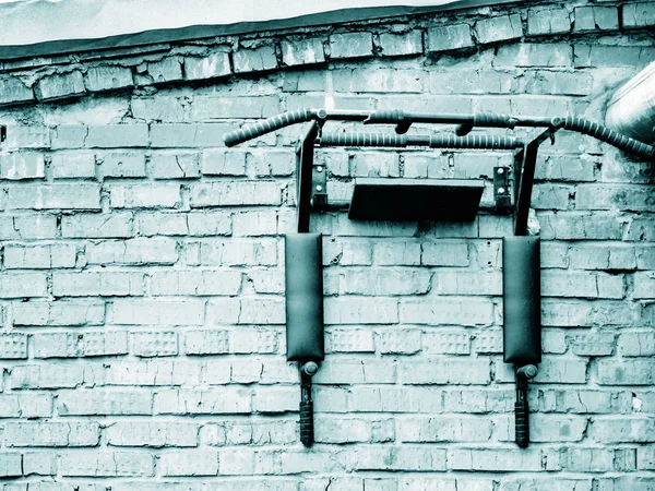 Kırmızı tuğlalı bir evin duvarına monte edilmiş bir spor çubuğu. Açık havada jimnastik aletleri