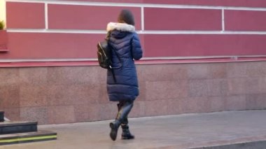 Koyu renk ceketle caddede koşuşturan genç bir kız figürü. Sırt çantalı kadın.