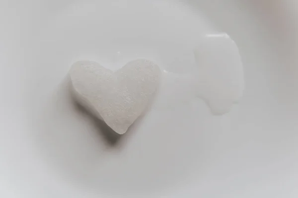 Śnieżne serce topi się na białym talerzu. Śnieg w kształcie serca na spodzie. Lód w mroźną pogodę. Stopiona woda zbierana jest w małej kałuży. Miłość na walentynki koncepcja — Zdjęcie stockowe
