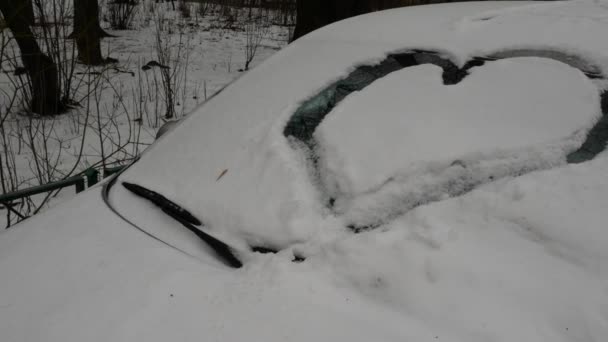 Símbolo del corazón dibujado en una capa de nieve en un coche. Un coche cubierto de nieve con un empate — Vídeos de Stock