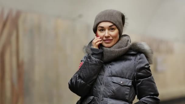 Ragazza con un telefono in giacca invernale sorride sulla piattaforma della stazione della metropolitana — Video Stock