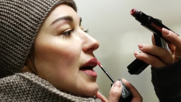 Jonge mooie vrouw met lippenstift borstel staat en kijkt naar spiegel — Stockvideo