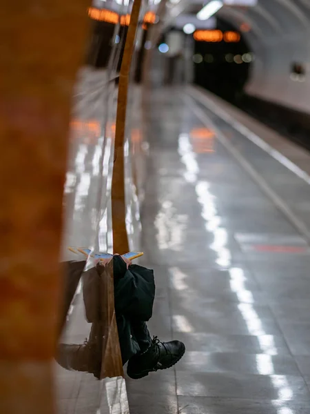 認識できない地下鉄の乗客が彼の手に携帯電話を持つ列車を待っています。女性は冬服でモスクワの地下鉄の車を待っている地下鉄のプラットフォーム上のベンチに座っています — ストック写真