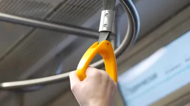 Dişi yolcu, metro vagonunda sallanan tırabzanları tutuyor.