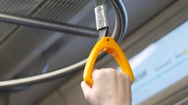Dişi yolcu, metro vagonunda sallanan tırabzanları tutuyor.