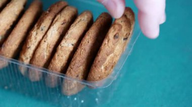 Yulaf ezmeli kurabiyeler şeffaf açık plastik tepside yatar. Erkek eli tatlı kurabiyeleri alır. Aşırı yeme ve karbonhidrat zengini gıdaları kötüye kullanma kavramı. Kan insülin seviyesini yükselten glisemik gıdalar