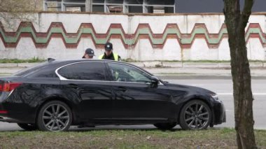 Polis devriyesi, durdurulan siyah arabanın sürücüsünün belgelerini kontrol ediyor.