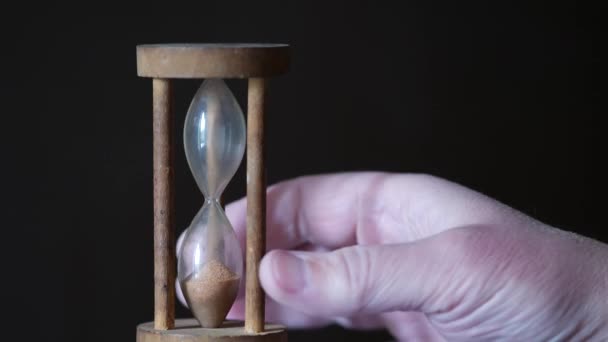 Una mano masculina voltea reloj de arena vintage antiguo sobre un fondo marrón oscuro — Vídeos de Stock