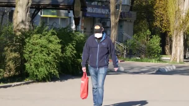 Ο άντρας φοράει μάσκα προσώπου ενώ περπατάει στο δρόμο την ανοιξιάτικη ηλιόλουστη μέρα — Αρχείο Βίντεο