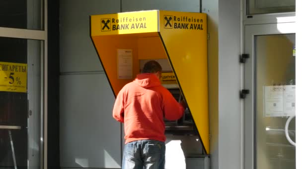 Homme en veste rouge est debout à la marque jaune Raiffeisen Bank Aval ATM — Video