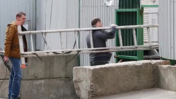 Mężczyźni bez masek z działającym narzędziem i drabiną przechodzą przez bramę. — Wideo stockowe