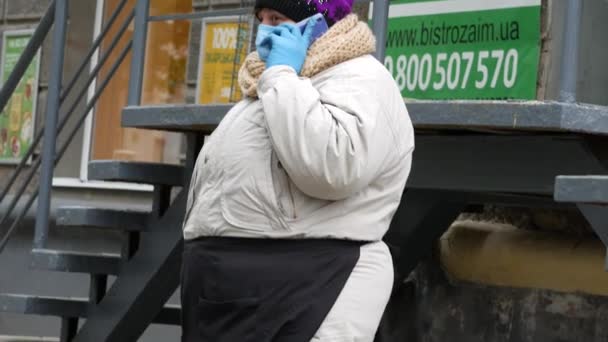 Chubby kobieta ulicy sprzedawca nosić maskę twarzy i niebieskie rękawiczki lateksowe podczas rozmowy telefonicznej — Wideo stockowe