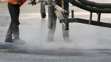 İşçiler yol kenarına asfalt çipleri püskürterek kaldırıma küçük onarımlar yapıyorlar
