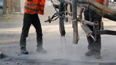 İşçiler asfalt çiplerini çukurlara püskürterek kaldırıma küçük onarımlar yapıyorlar.