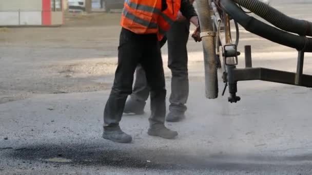 Рабочие выполняют незначительный ремонт тротуара, распыляя асфальтовые стружки на дорогах. — стоковое видео