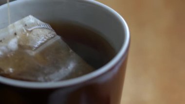 Çay poşeti, kahvaltı için kahverengi bir porselen bardağa dökülen kaynar suda yüzer.