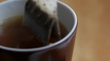 Çay poşeti, kahvaltı için kahverengi bir porselen bardağa dökülen kaynar suda yüzer.