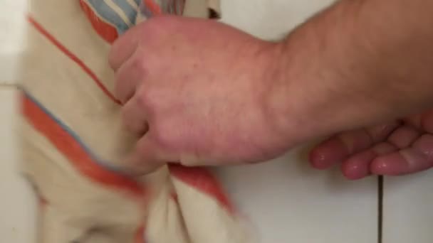 Ręcznik wisi przy białym kafelku. Mężczyzna wyciera swoje mokre ręce na ręcznik kuchenny — Wideo stockowe