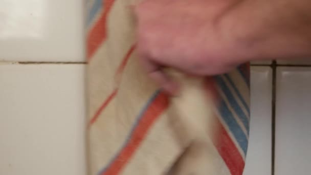 Handdoek hangt in de buurt van witte betegelde muur. man veegt zijn natte handen op keukendoek — Stockvideo