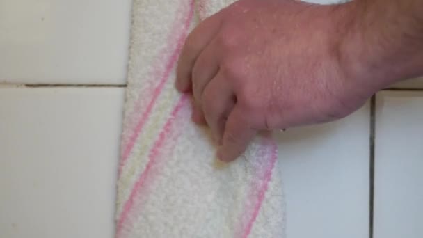 Handtuch hängt neben weiß gekachelter Wand. Mann wischt sich nasse Hände auf Küchentuch — Stockvideo