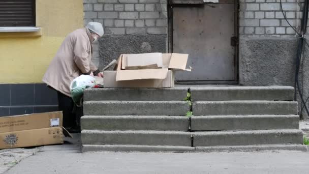 Пожилая женщина пенсионного возраста в защитной маске сортирует гофрированный картон — стоковое видео