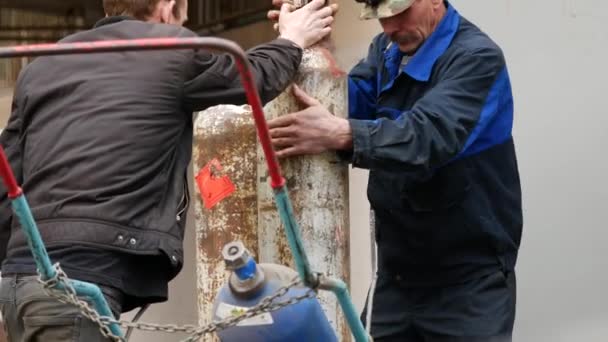 Workers change acetylene gas tank in warehouse. Welder with cigarette in mouth — Stock Video