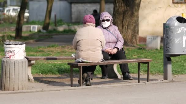 Le donne anziane sedute sulla panchina indossano maschere facciali e parlano. Quarantena — Video Stock