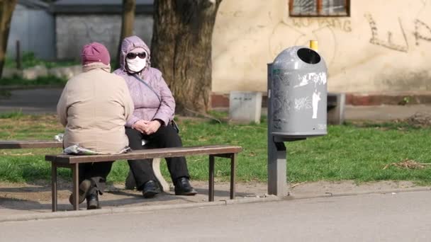 ストリートベンチに座っている高齢者の女性は顔マスクを着用し、話をする。隔離 — ストック動画