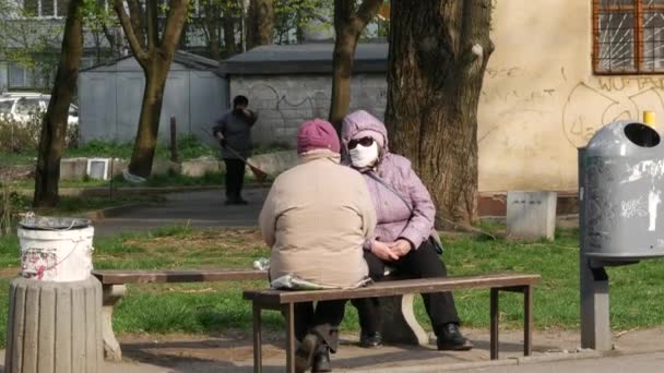 Oudere vrouwen die op een bankje zitten dragen gezichtsmaskers en praten. Quarantaine — Stockvideo