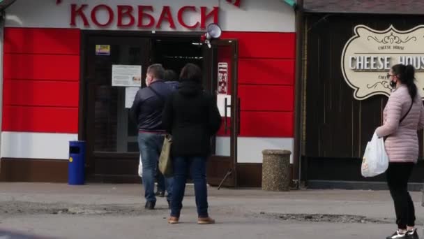 Mensen observeren sociale afstand en rij op straat in de buurt van de ingang van de supermarkt — Stockvideo