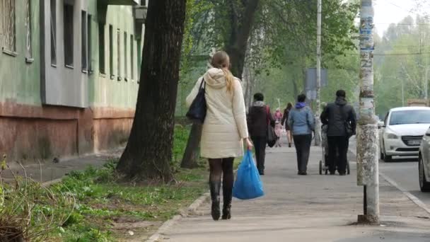 Egy fekete csizmás hölgy és egy könnyű, szezonon kívüli kabát egy kék műanyag zacskót hordoz. — Stock videók