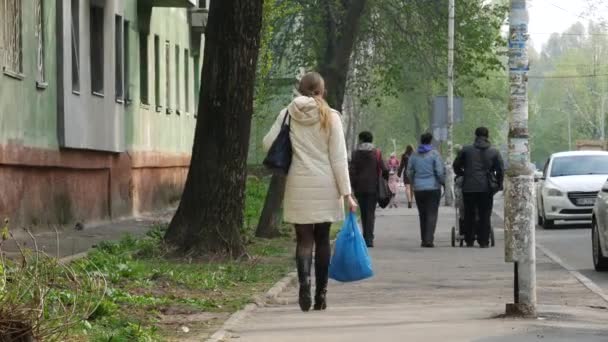 Lady in zwarte laarzen en een lichte jas buiten het seizoen draagt een blauwe plastic zak — Stockvideo