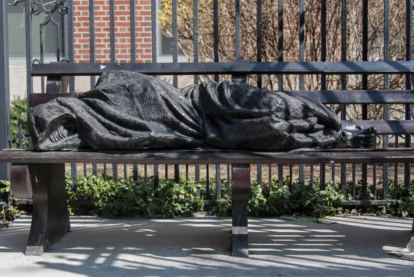 Homem sem-teto dormindo em uma estátua de banco — Fotografia de Stock