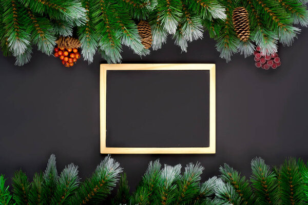 Christmas or New Year decoration on dark background: fir-tree branches, winter berries on branch and drawing board. Banner mockup, postcard. Flat lay, top view