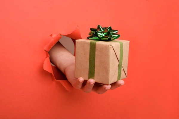 Hand geven rood en wit gestreepte geschenkdoos op gescheurde rode papieren muur. Kopieer ruimte apart voor uw reclame en aanbod of verkoop inhoud. — Stockfoto