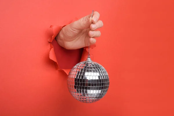 Ręczne trzymanie kuli lustrzanej Silver Disco na podartej czerwonej papierowej ścianie. Odłóżmy na bok miejsce na reklamę i ofertę lub treść sprzedaży. — Zdjęcie stockowe