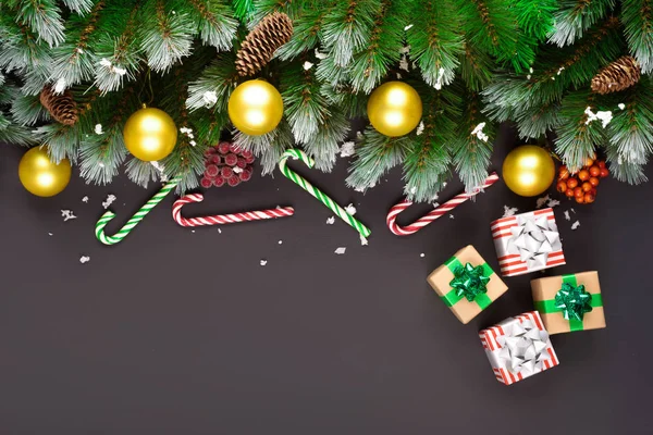 С Новым годом или Рождеством! Ветви ели, рождественские игрушки, подарочная коробка, пушистый снег, сосновые шишки, конфеты и зимние ягоды на черном фоне. Плоская кладка, копируйте пространство для вашего текста . — стоковое фото