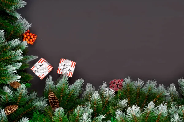З Різдвом або з Новим роком. Ялинкові гілки, різдвяні іграшки, подарункова коробка, пухнастий сніг, соснові шишки, цукерки та зимові ягоди на чорному тлі. Плоский простір для тексту . — стокове фото