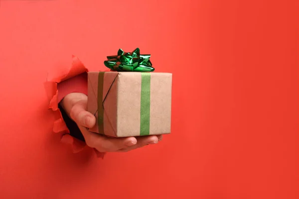 Main donner boîte cadeau rayé rouge et blanc sur le mur de papier rouge déchiré. Espace de copie réservé à votre publicité et à votre contenu d'offre ou de vente . — Photo