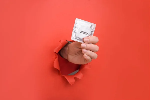 Hand geven condoom op gescheurde rode papieren muur. Veilig plezier en bescherming, anticonceptie, bescherming tegen aids en dag om aids te bestrijden. Kopieer ruimte opzij voor uw reclame-inhoud — Stockfoto